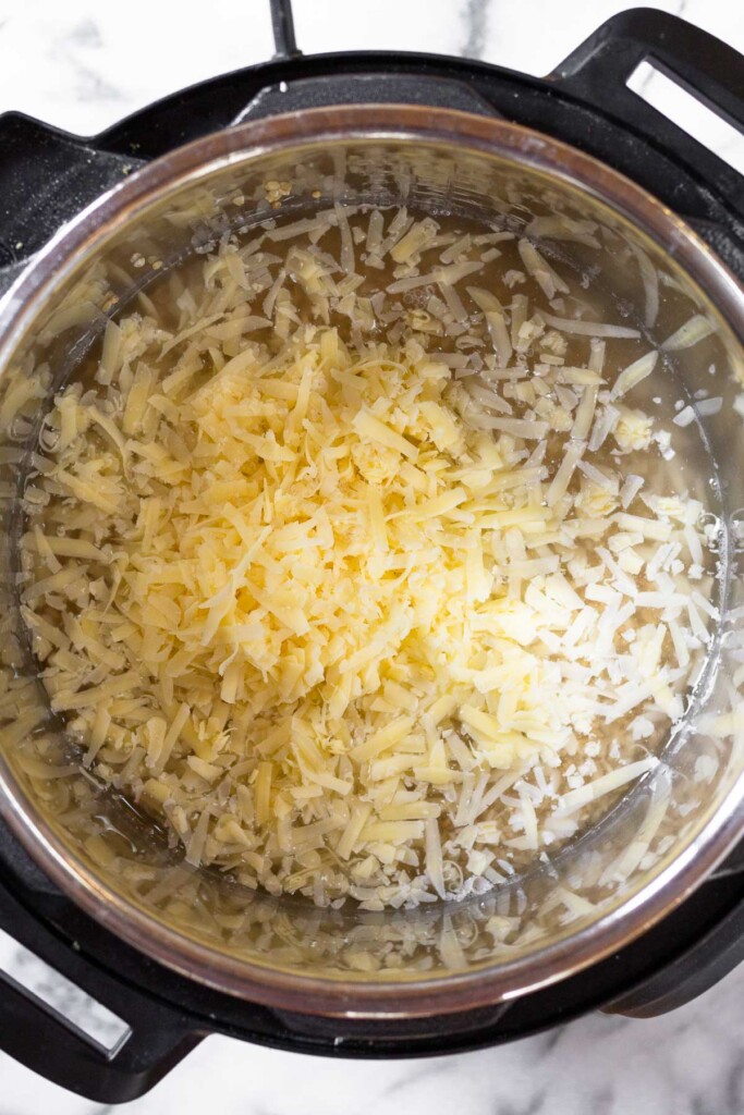 Instant pot filled with rice, water, and shredded cheese.