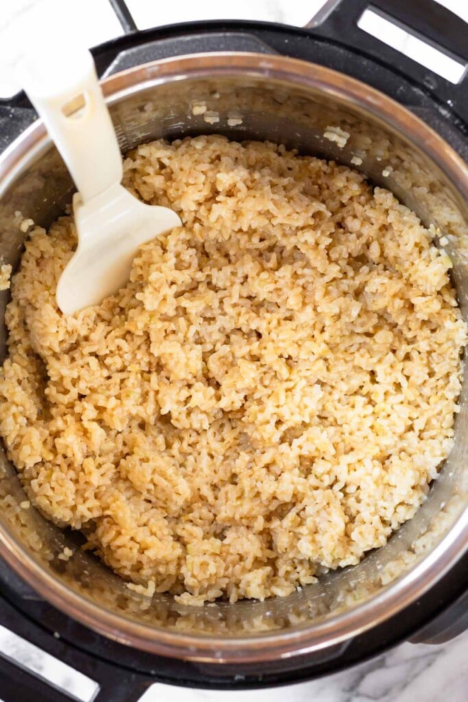 Instant pot filled with cheesy brown rice with a plastic spoon in it.