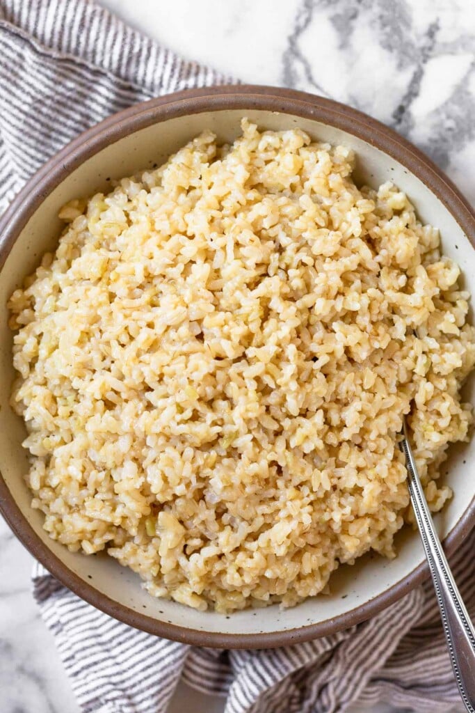 Cheesy brown rice in a large bowl with a spoon in it. The bowl is on top of a striped towel.