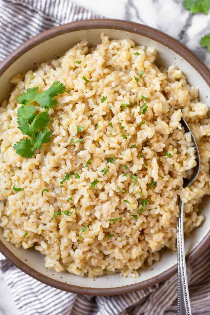 Overhead shot of cheesy rice in a large white bowl garnished with cilantro. There is a spoon in the bowl and the bowl is on a striped kitchen towel.