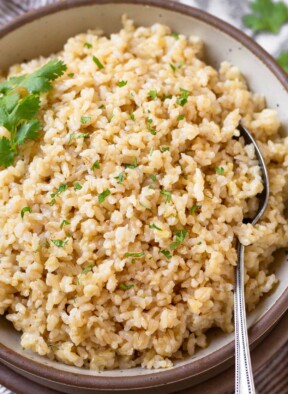 Close up of a bowl of cheese rice garnished with cilantro. A spoon is also in the bowl.