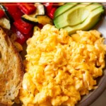 A close up a a plate with cottage cheese scrambled eggs, toast, sautéed veggies, and avocado.