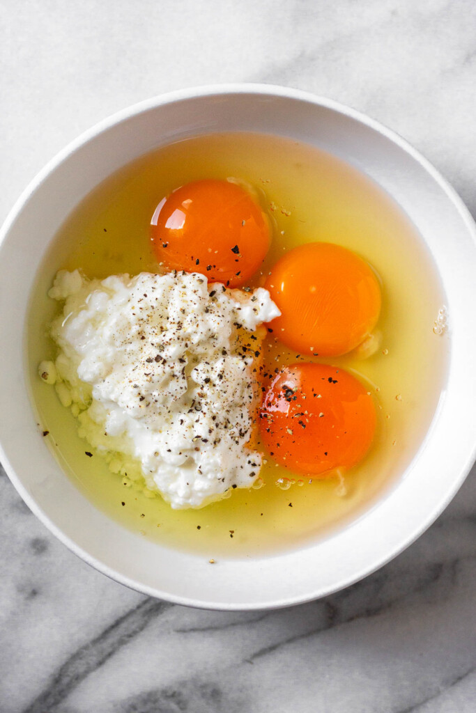 White bowl with 3 eggs and cottage cheese in it. Some black pepper is sprinkled on top.