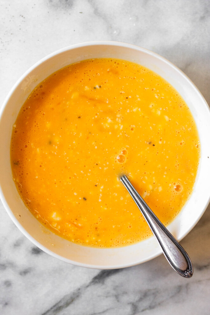 A bowl with scrambled eggs in it. A fork is also in it.