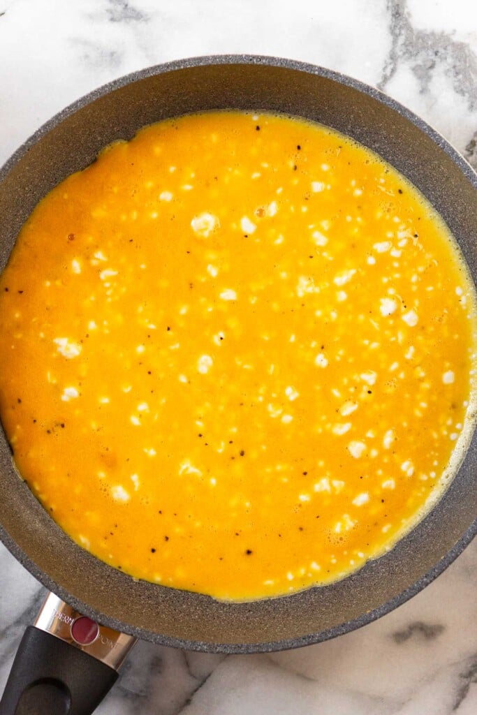 Overhead shot of a large skillet with cottage cheese in scrambled eggs spread across the bottom before they are cooked.