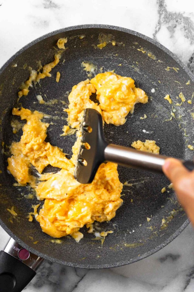 Large skillet filled with scrambled eggs with a spatula moving them around as they cook.