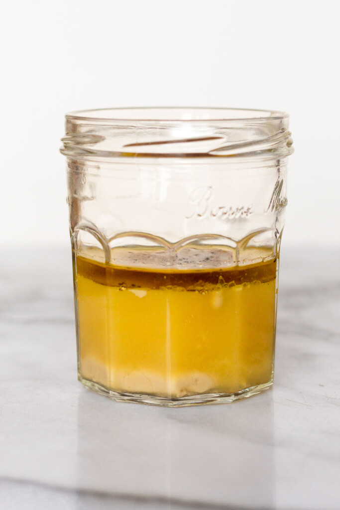 Straight on shot of a glass jar filled with tahini, orange juice, olive oil, vinegar, and spices.