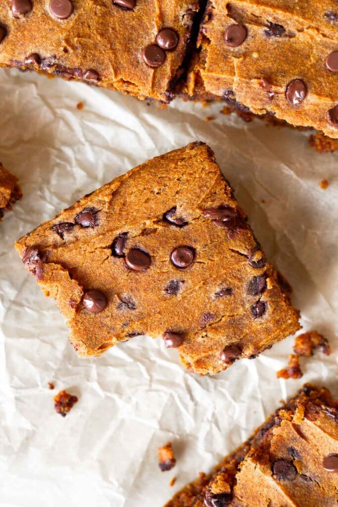 Overhead shot of pumpkin chocolate chip bars on a piece of parchment paper. One has a bite out of it with crumbs around it.