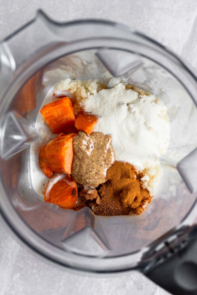 Overhead shot of a blender with frozen sweet potatoes pieces, frozen cauliflower rice, collagen, almond butter, and spices in it.
