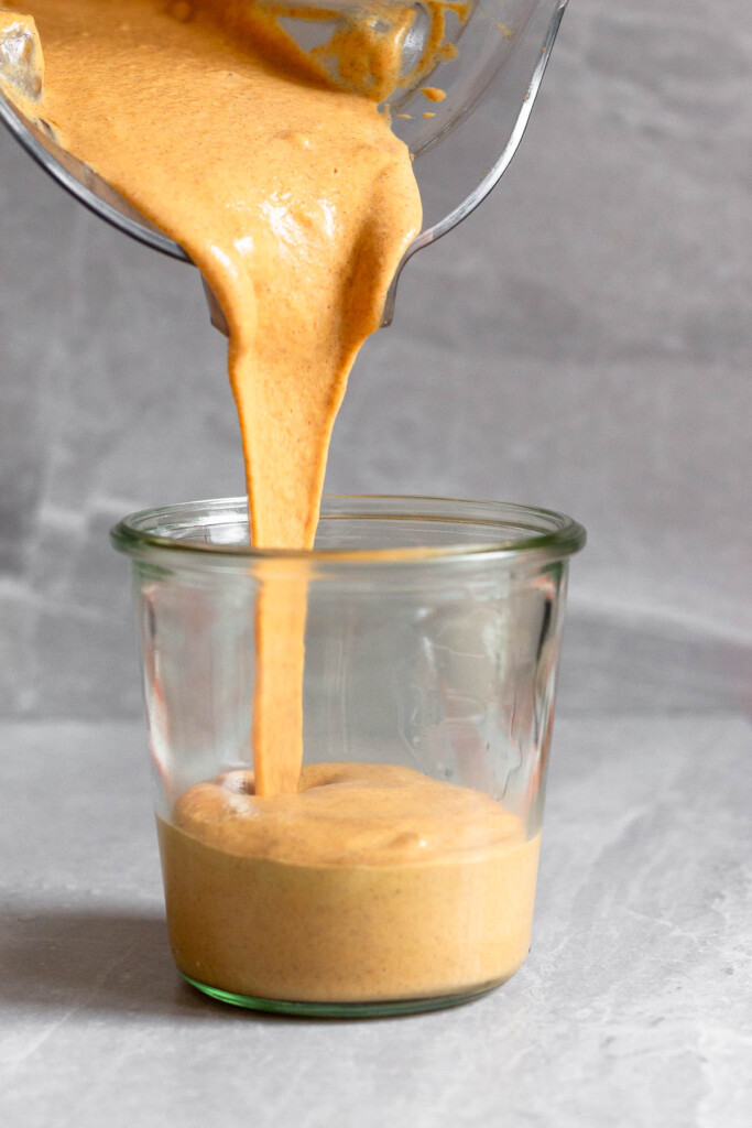 Thick and creamy orange smoothie being poured into a large glass.
