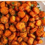 Air fryer roasted carrots on a white plate topped with fresh herbs.