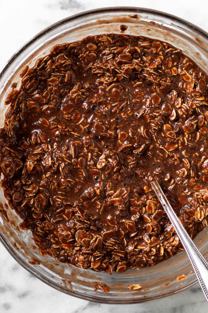 Glass bowl with a chocolate batter with rolled oats and chocolate chips in it. A fork is in the bowl.