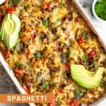 Overhead shot of spaghetti squash casserole in a large casserole dish. It is topped with sliced avocado and cilantro. Next to it is a bowl of corn chips, bowl of cilantro, and half an avocado.