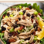 Cranberry pecan chicken salad overtop some greens in a bowl and garnished with 2 lemon wedges.