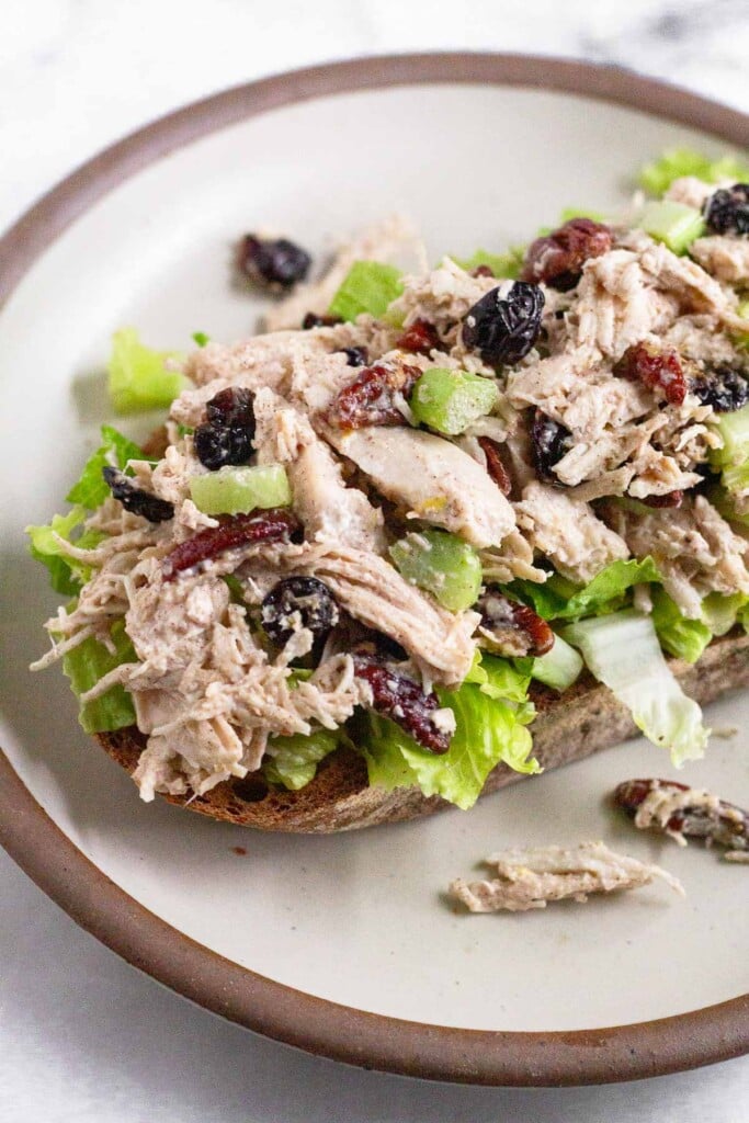 Chicken cranberry pecan salad on top of some lettuce on a piece of toast on a white plate.