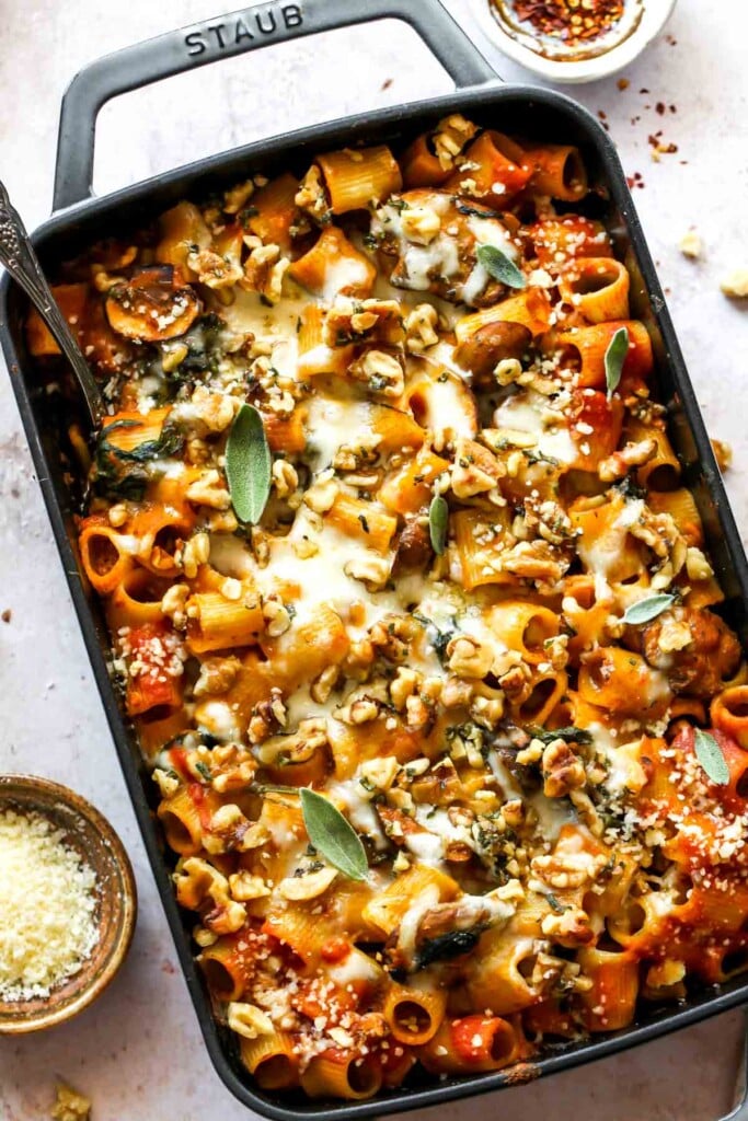 Overhead shot of a large baking dish with pasta and sauce topped with melted cheese. A spoon is in the pan and it is garnished with fresh sage.