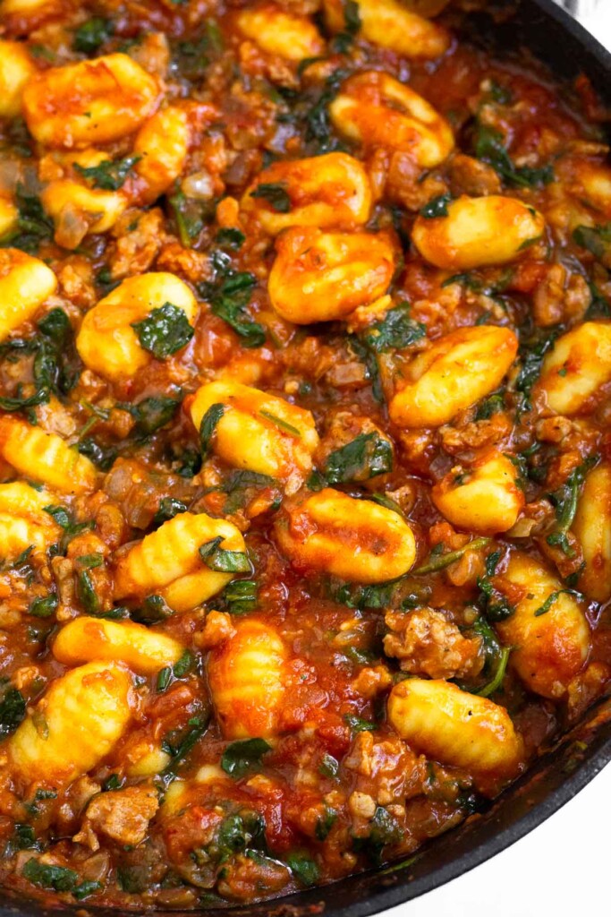Gnocchi and sausage mixed in pasta sauce with spinach in a large skillet.