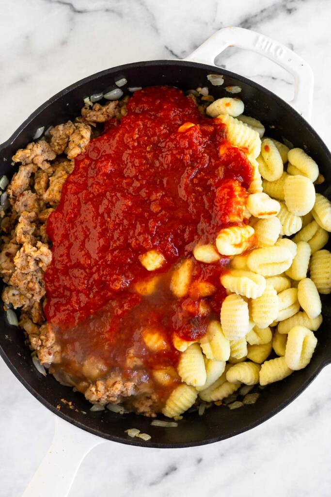 Large skillet with cooked sausage, uncooked gnocchi, pasta sauce, and chicken broth in it before it is mixed up.