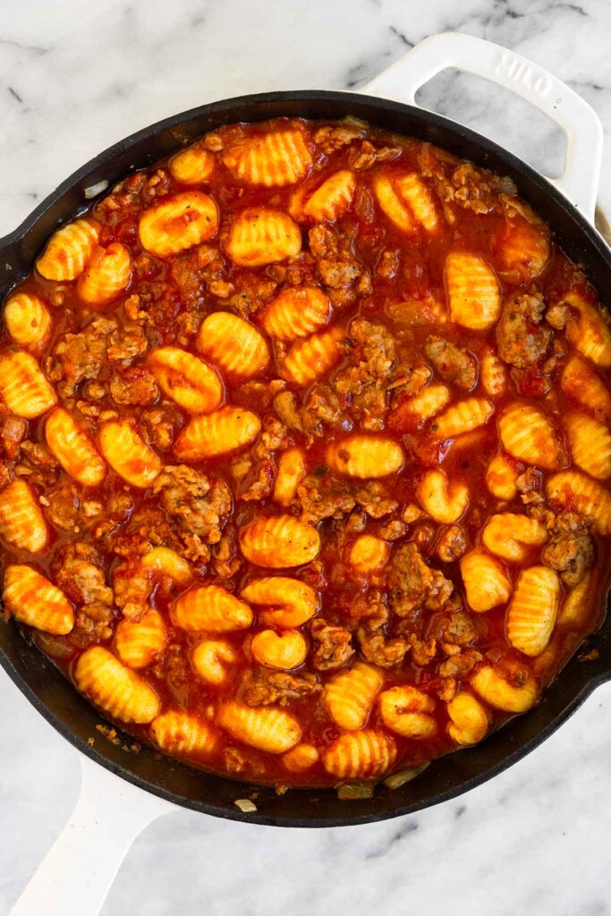 Overhead shot of a large skillet with sausage and gnocchi mixed together with pasta sauce.