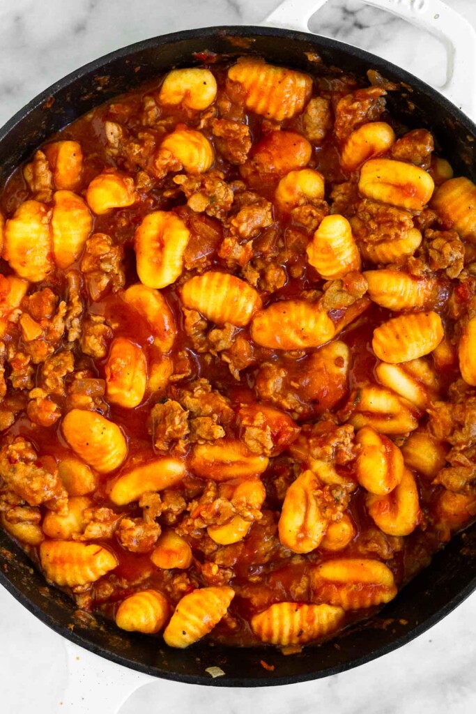 Large skillet with sausage and gnocchi in pasta sauce.