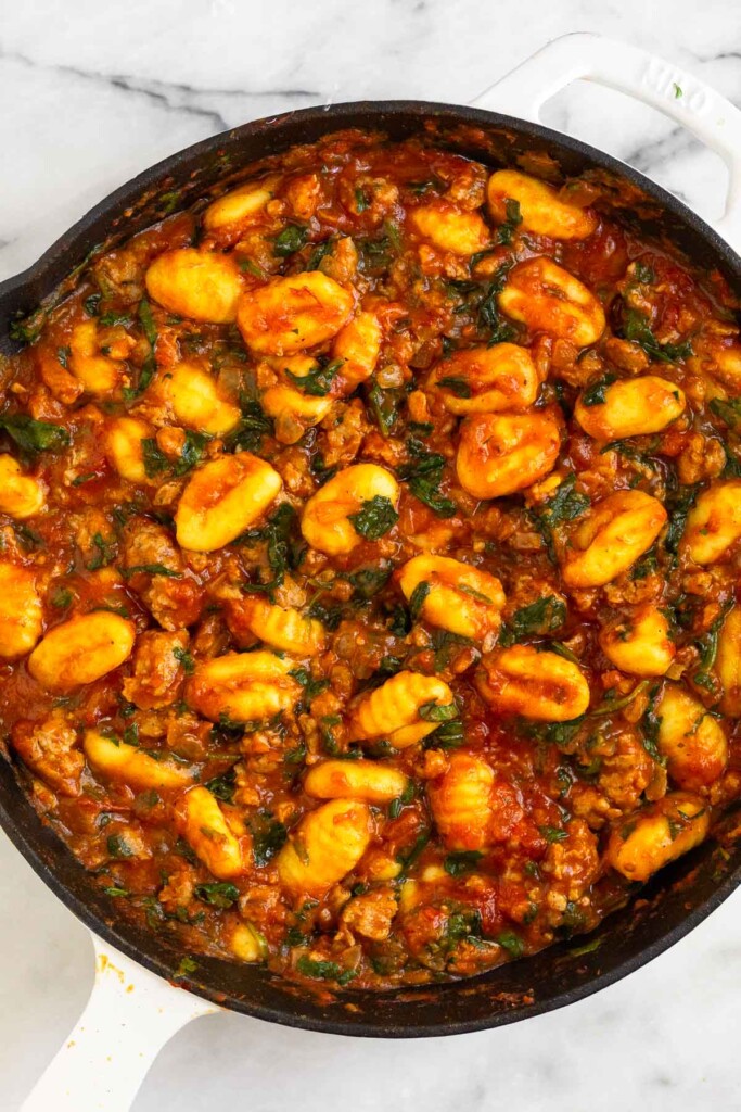Large skillet with gnocchi, sausage, and spinach in pasta sauce.