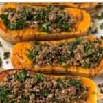 Ground beef stuffed butternut squash with kale and drizzled with tahini sauce on a baking sheet.