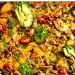 Large cast iron skillet with chicken fajita casserole with rice and topped with melted cheese. It is garnished with sliced avocado, jalapeños, and cilantro.