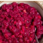 White bowl of homemade cranberry sauce with a spoon in it.