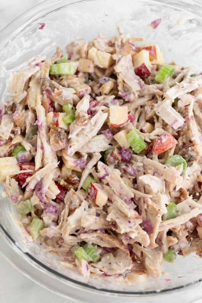 A large glass bowl of turkey salad with apples, celery, cranberries, and walnuts in it.