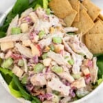 Leftover turkey salad with apples and celery in a bowl with some crackers overtop some greens. Behind the bowl is another bowl with similar contents.
