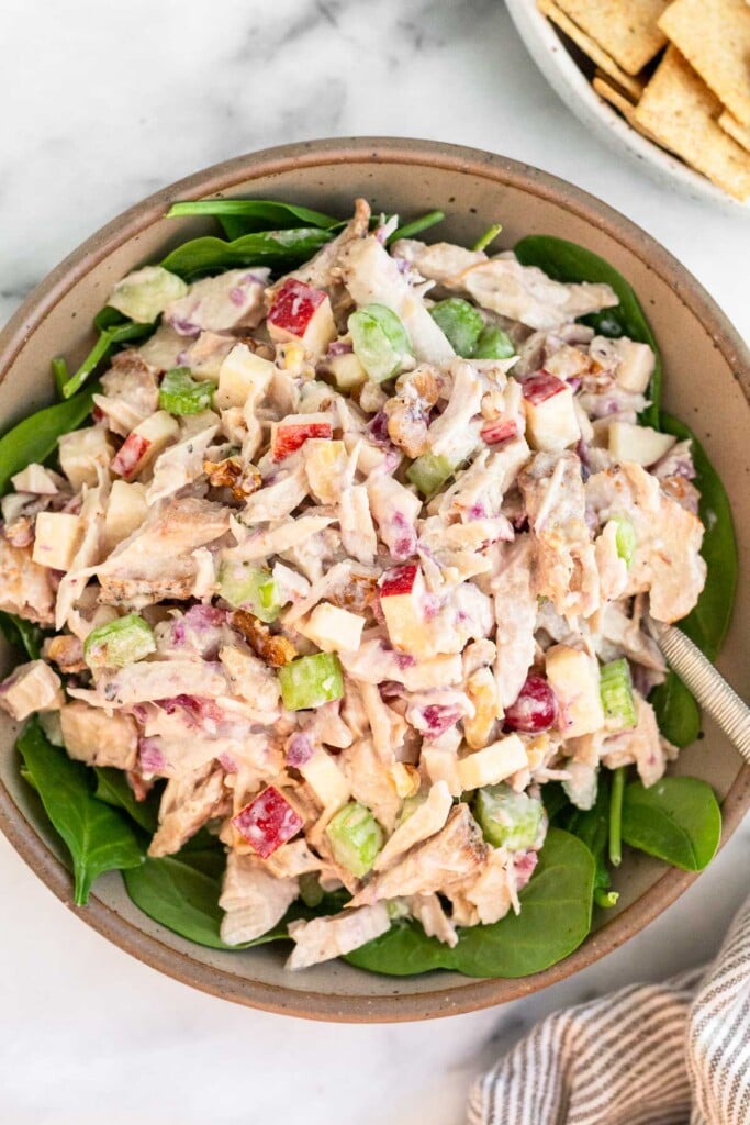 Large bowl of turkey salad overtop greens. Next to the bowl is a side of crackers.