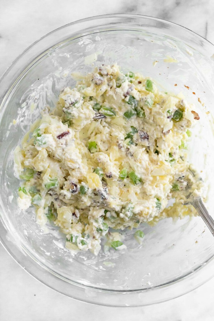 A bowl filled with a mixture of cream cheese, pineapple, onion, green pepper, and nuts.