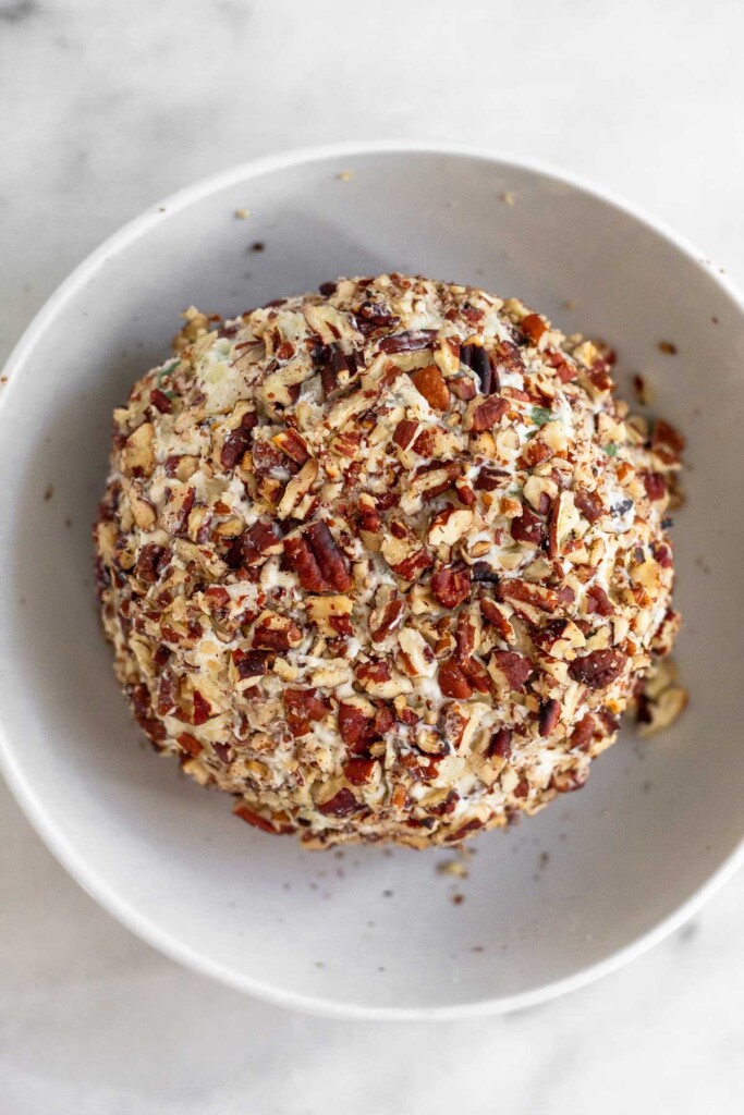 Overhead shot of a cream cheese ball coated with chopped nuts in a white bowl.