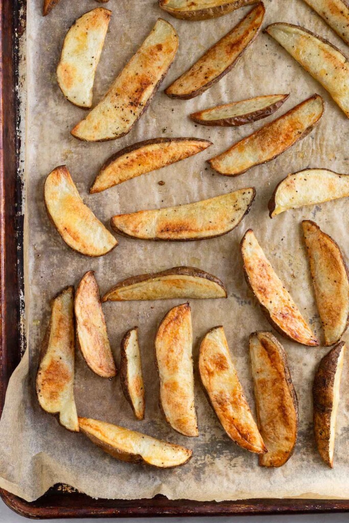 Oven baked potato wedges on a baking sheet lined with parchment paper.