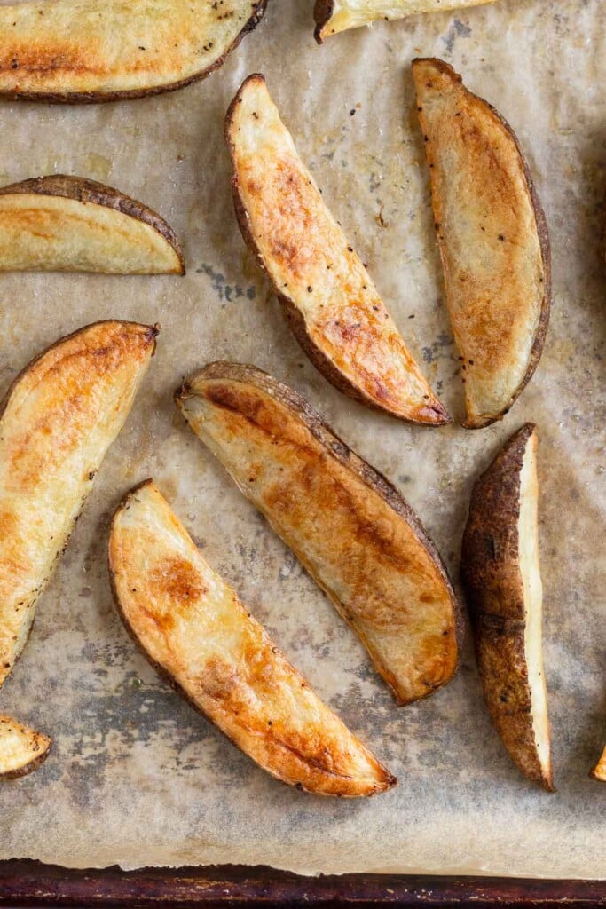 Close up of homemade potato wedges on a parchment paper linked baking sheet.