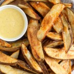 Baked potato wedges piled on a plate with a ramekin of honey mustard.