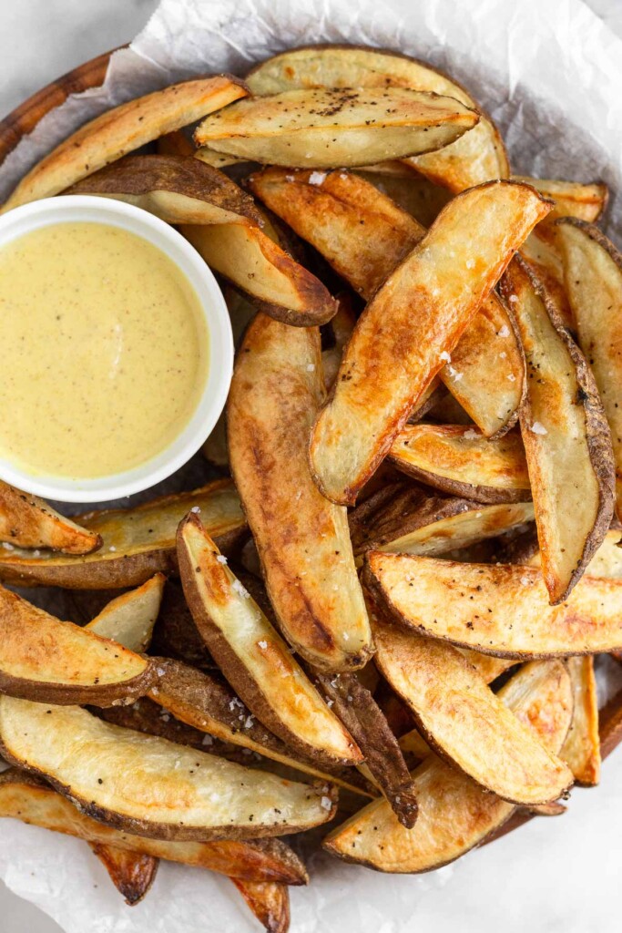 Baked potato wedges piled on a plate with a ramekin of honey mustard.