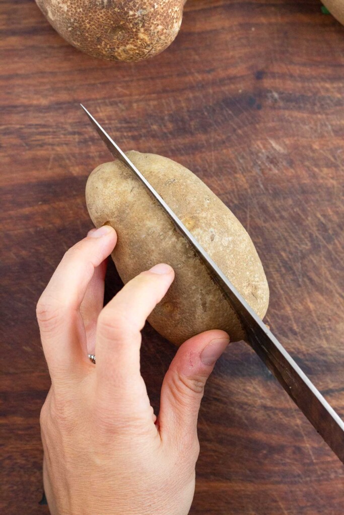 Overhead shot of someone cutting a russet potato in half lengthwise.