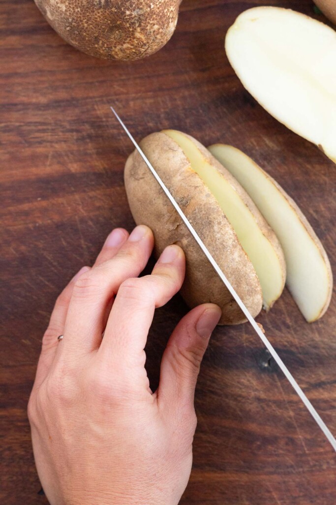Overhead shot of someone cutting a half of a russet potato into wedges.
