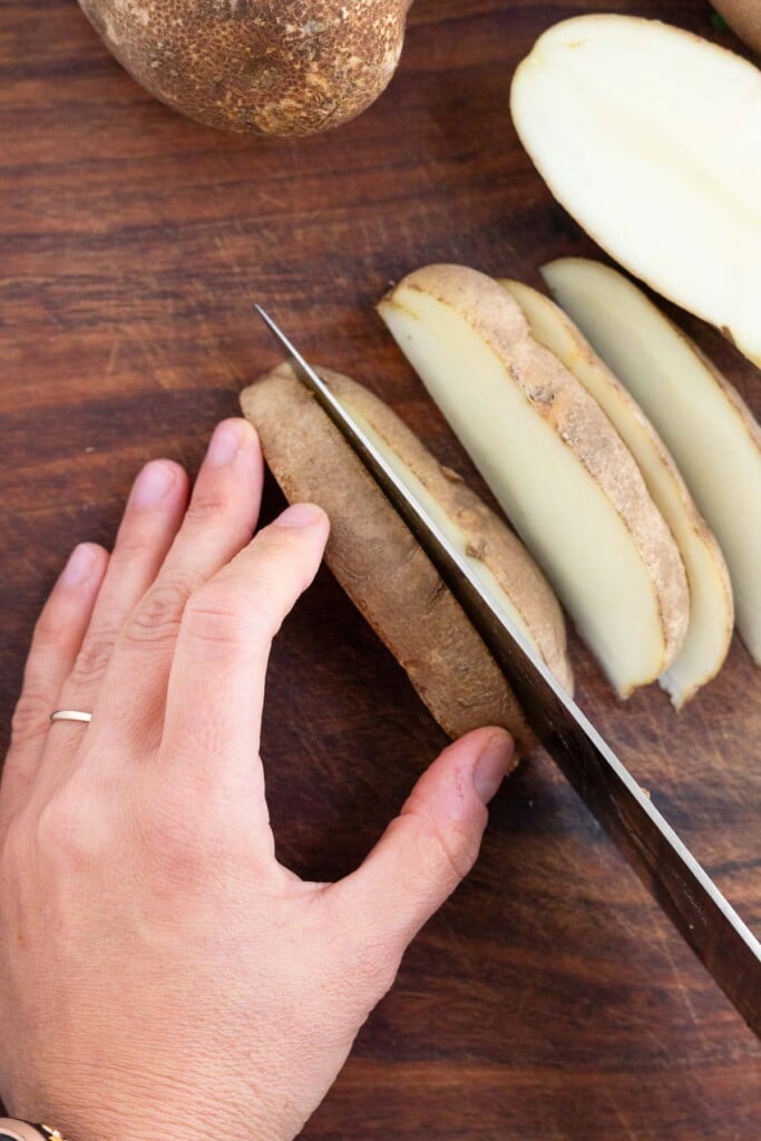 Overhead shot of someone cutting a half of a russet potato into potato wedges.