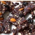 Sheet pan of pieces of chocolate bark with almonds, dried cherries, and shredded coconut sprinkled with flaky sea salt.