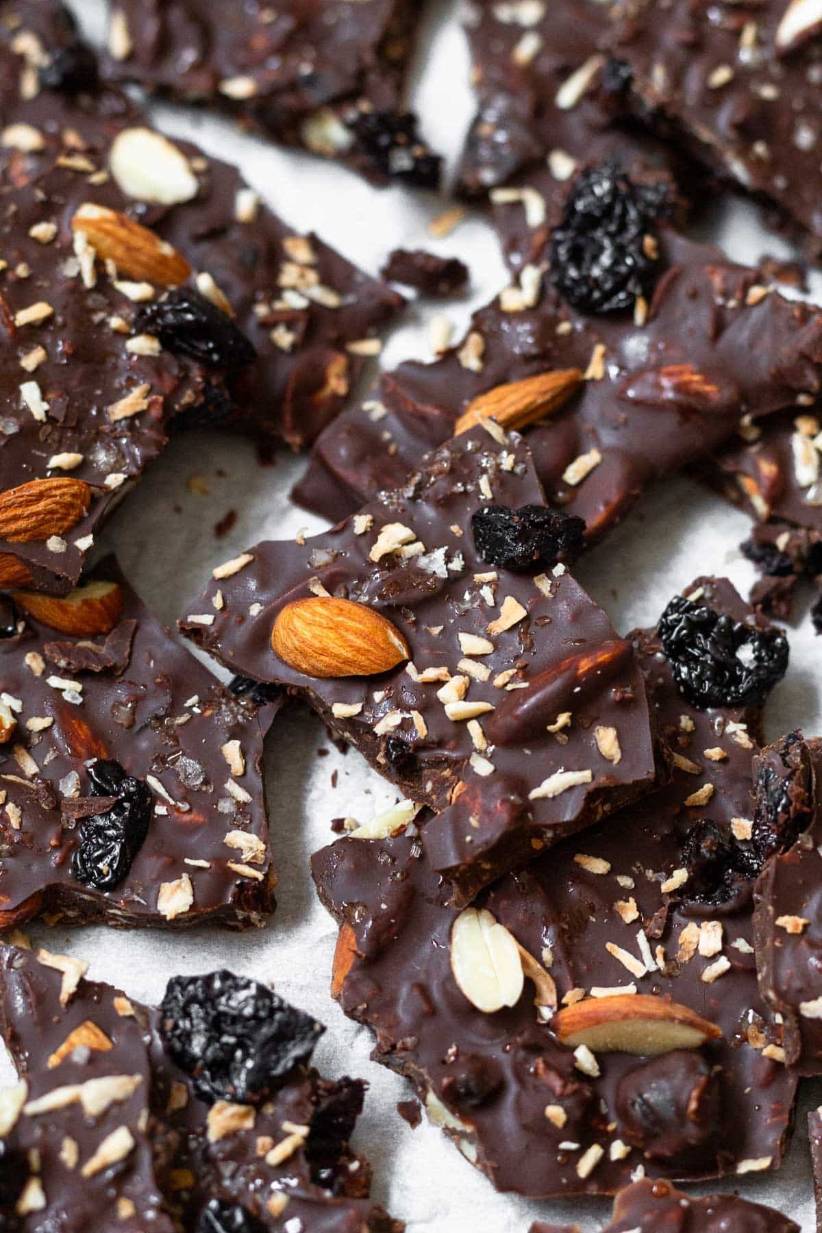 Sheet pan of pieces of chocolate bark with almonds, dried cherries, and shredded coconut sprinkled with flaky sea salt.