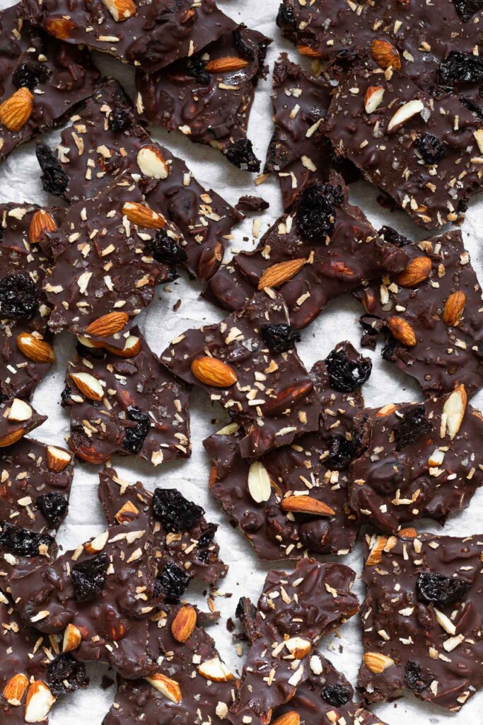 Overhead shot of a baking sheet with a bunch of pieces of chocolate almond bark with dried cherries and shredded coconut.