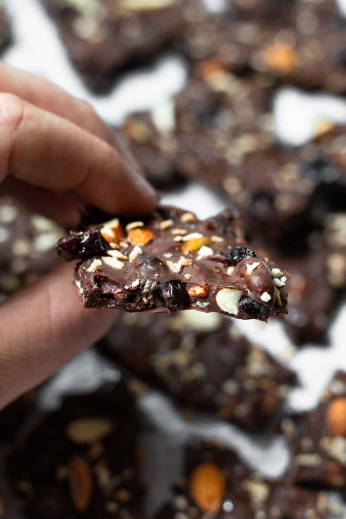 A bunch of pieces of almond chocolate bark on a baking sheet with dried cherries, coconut. It is sprinkled