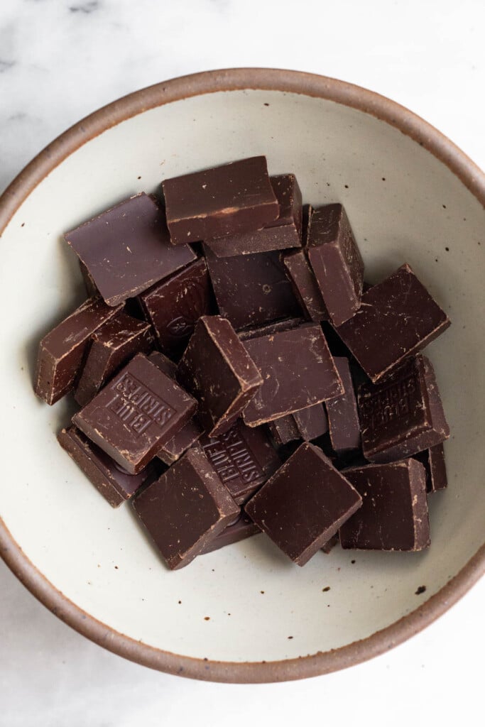 White bowl with squares of dark chocolate in it.