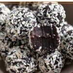 A bowl of chocolate peppermint energy balls coated with shredded coconut. One of them as a bite taken out of it.