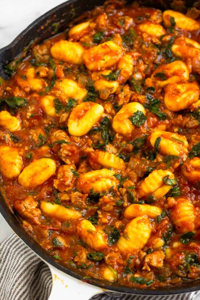 Healthy one pan meal with sausage, gnocchi and spinach mixed with pasta sauce in a large skillet.