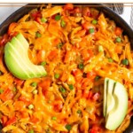 Buffalo chicken casserole topped with melted cheese in large cast iron skillet. It is garnished with sliced avocado and green onions.