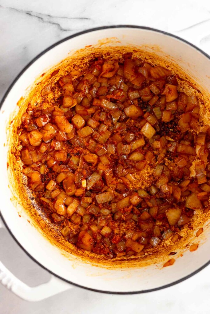 A mixture of sautéed onions, garlic, and tomato paste in a white dutch oven.
