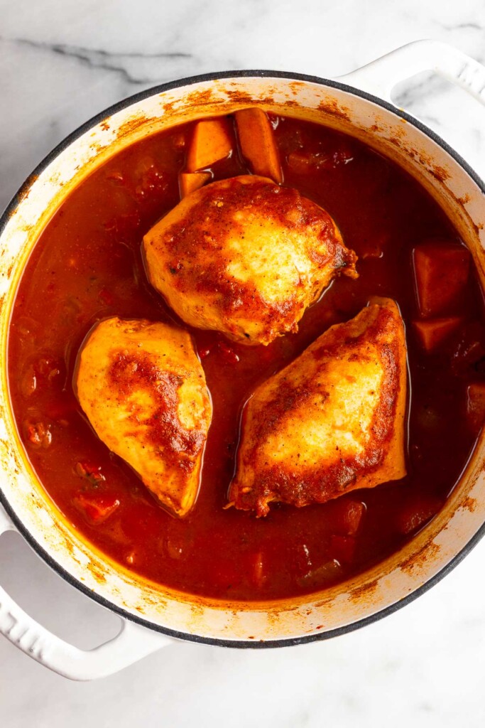 Cooked chicken breasts with veggies and broth in white dutch oven.